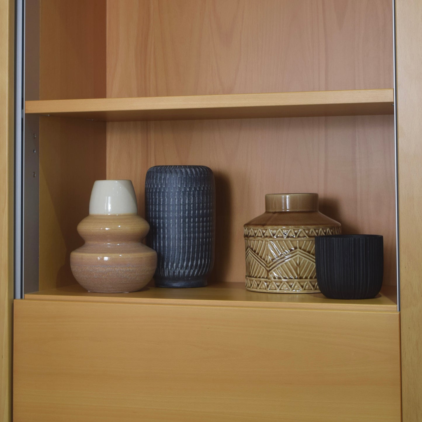 Four decorative vases on a wooden shelf for shelf styling