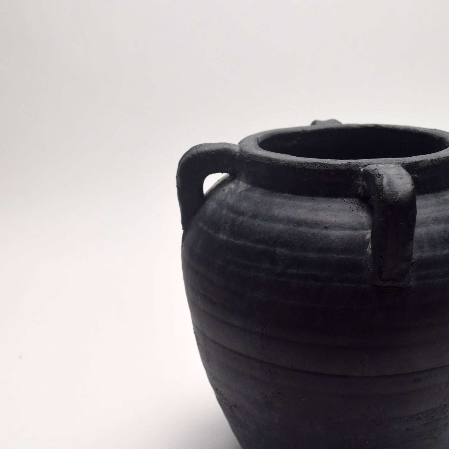 Black ceramic vase with small decorative handles on a white background