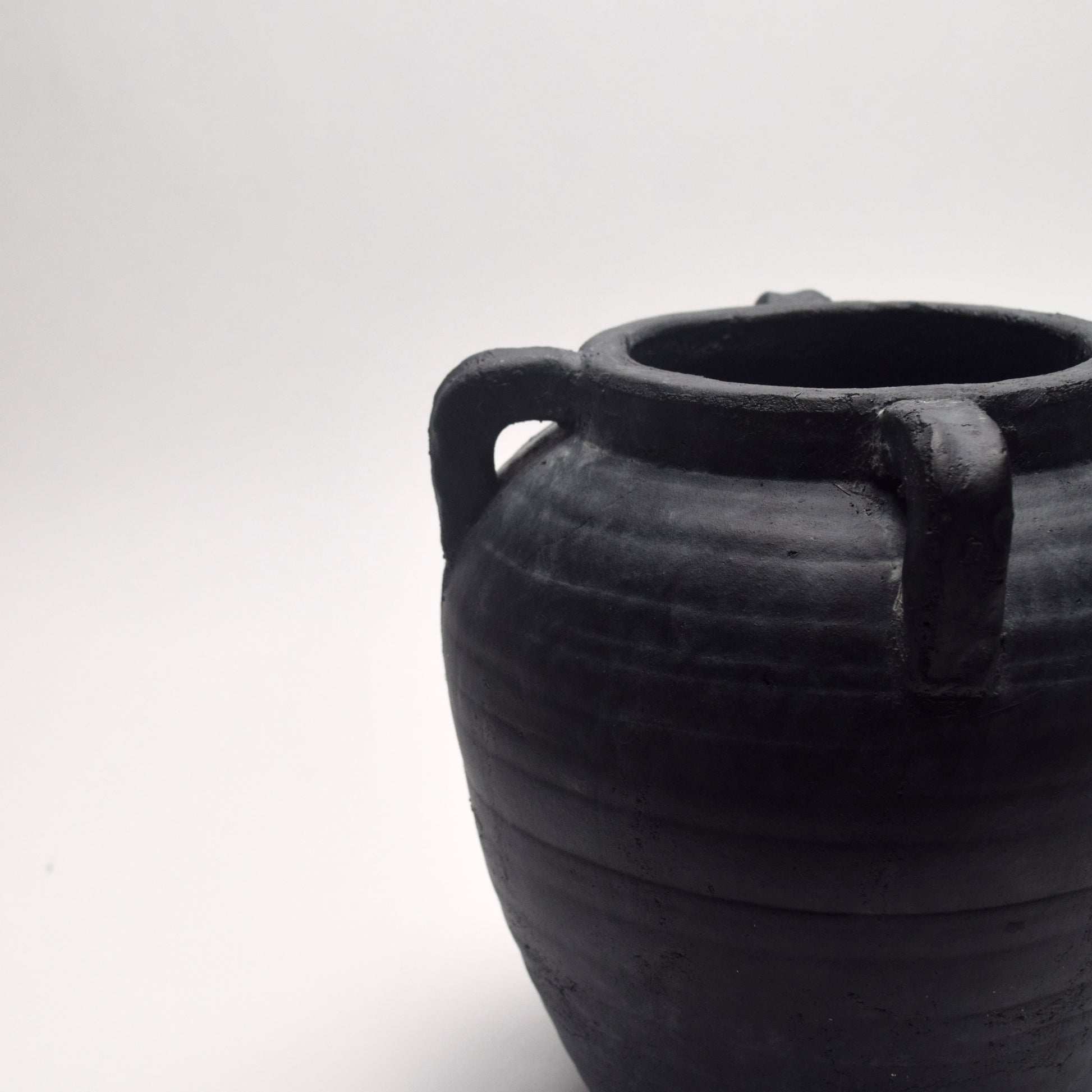 Black ceramic vase with small decorative handles on a white background