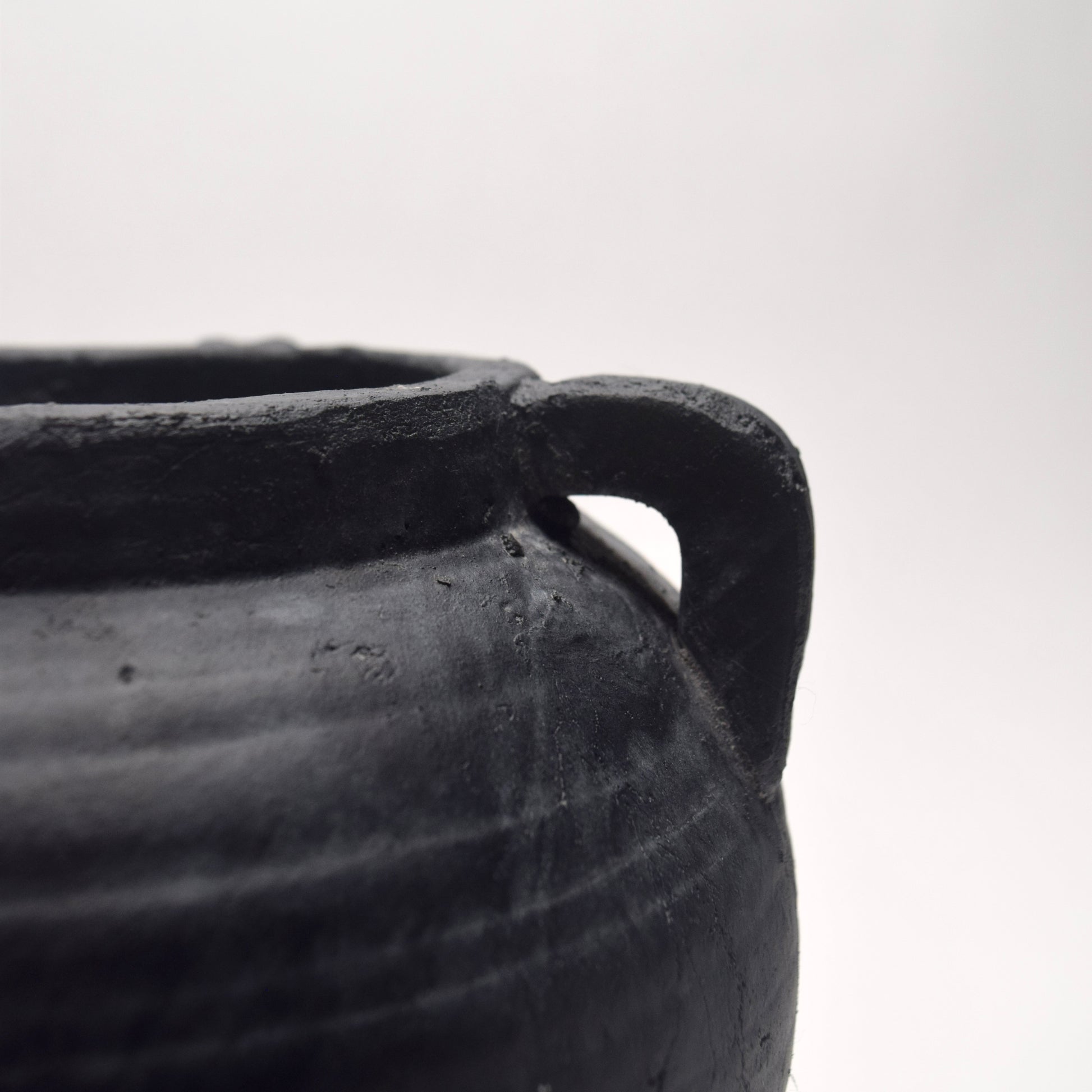 Close-up of a black ceramic pot with a handle and rustic textured surface