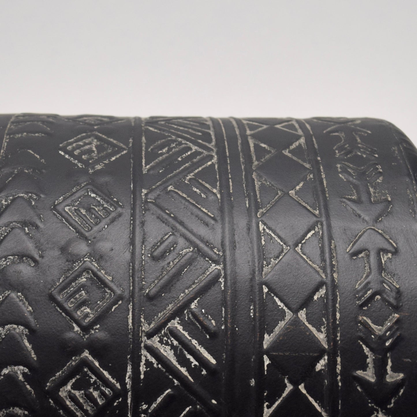 Close-up of a black cylindrical vase with geometric, aztec white patterns 