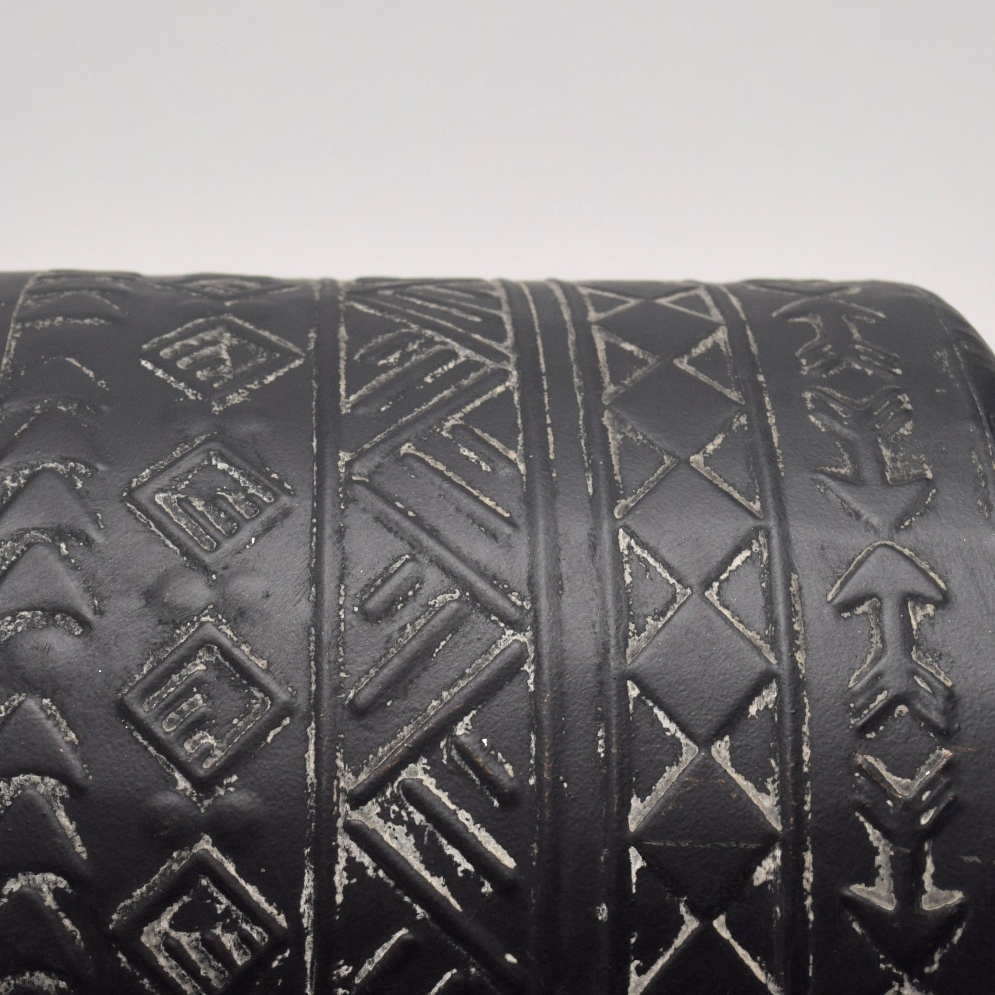 Close-up of a black cylindrical vase with geometric, aztec white patterns 