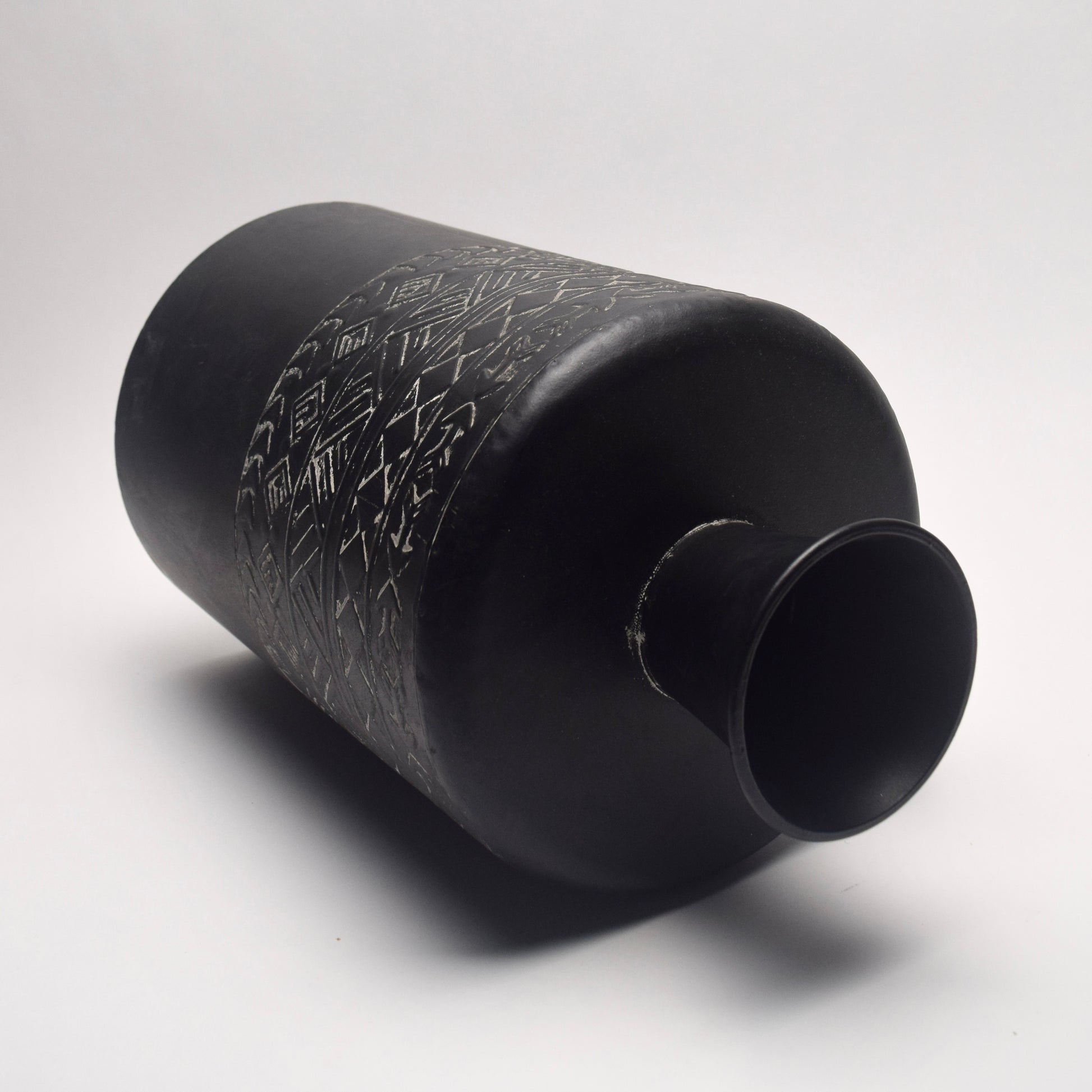 Black metal vase on its side with textured geometric patterned surface 