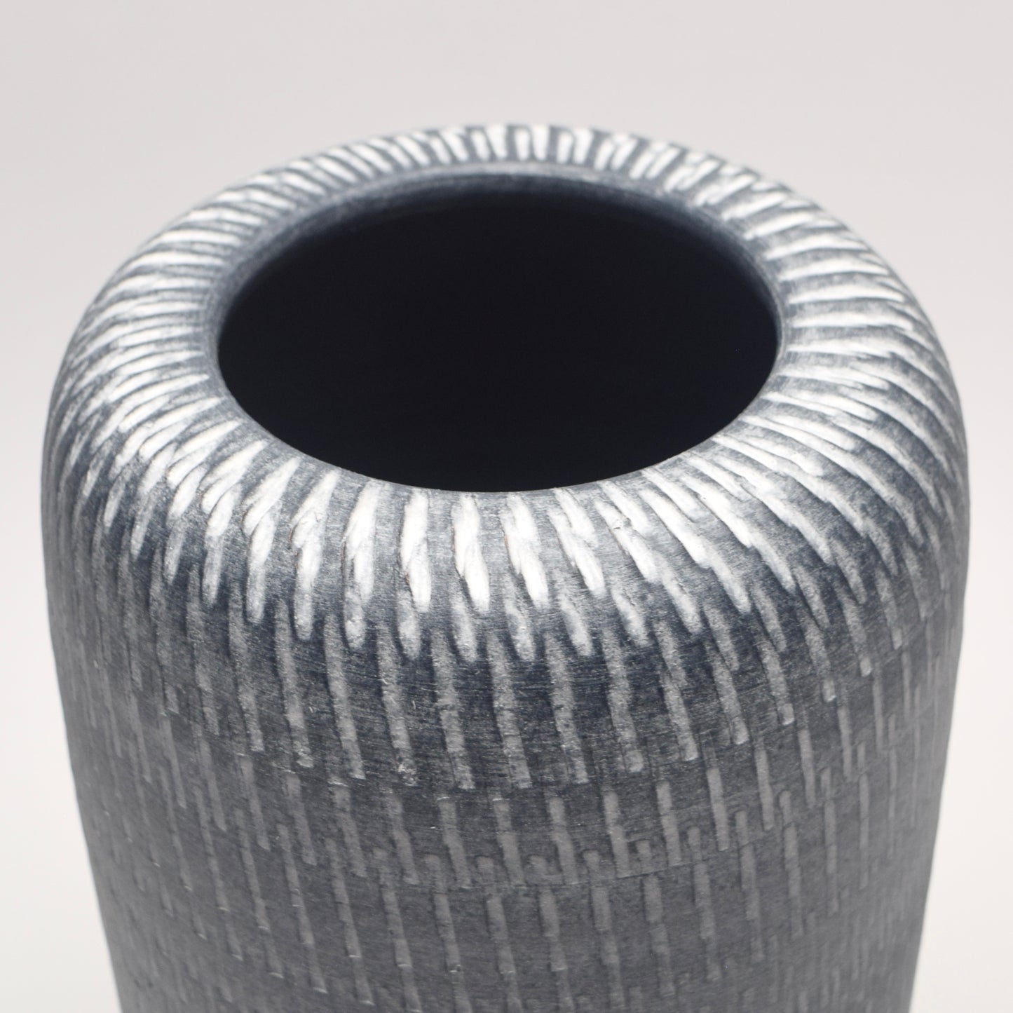 Linear white pattern on a grey pillar shaped terracotta vase 