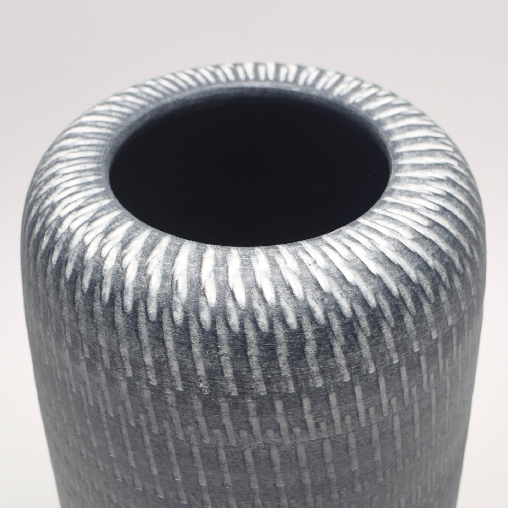Linear white pattern on a grey pillar shaped terracotta vase 