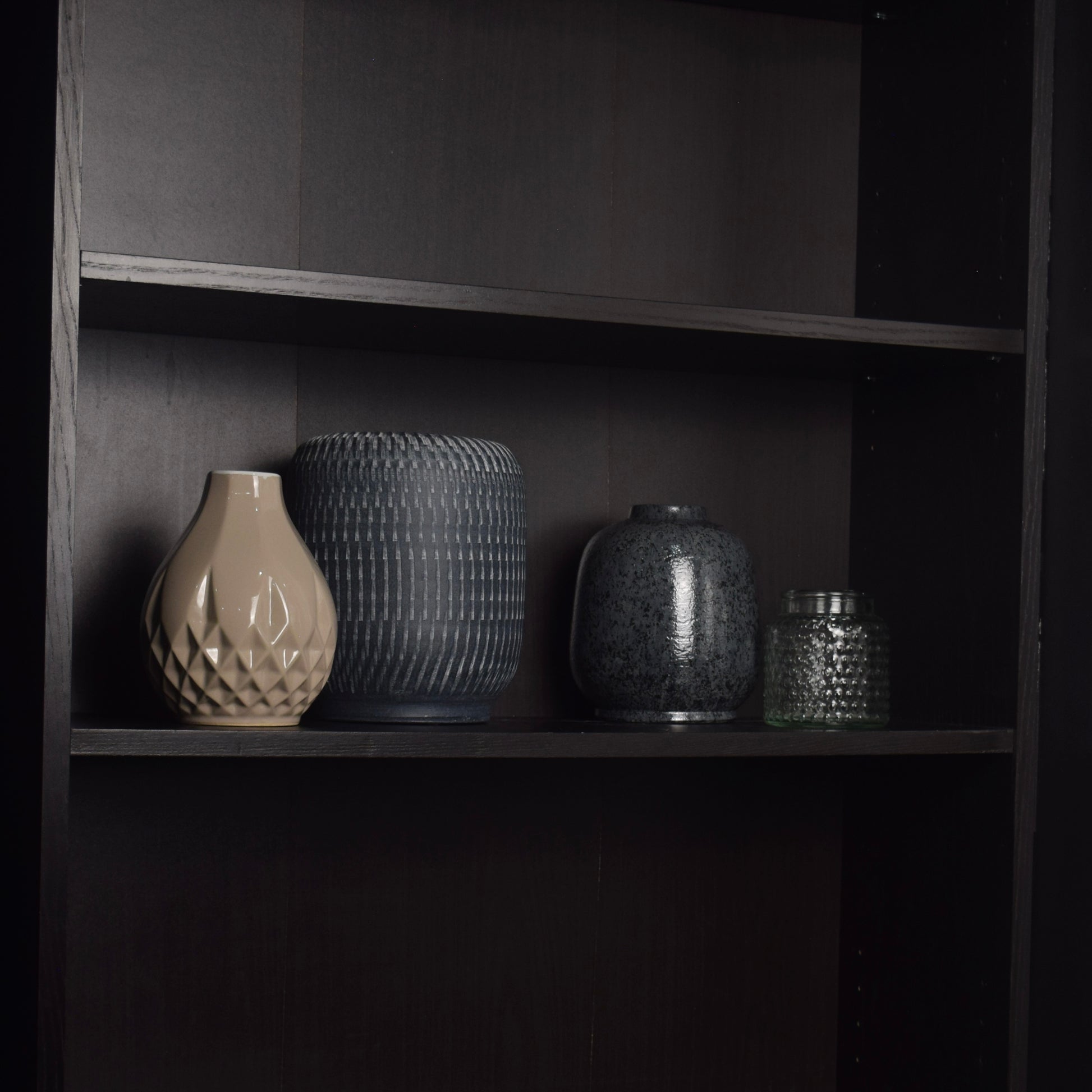 Set of four ceramic vases on black bookcase for shelf styling
