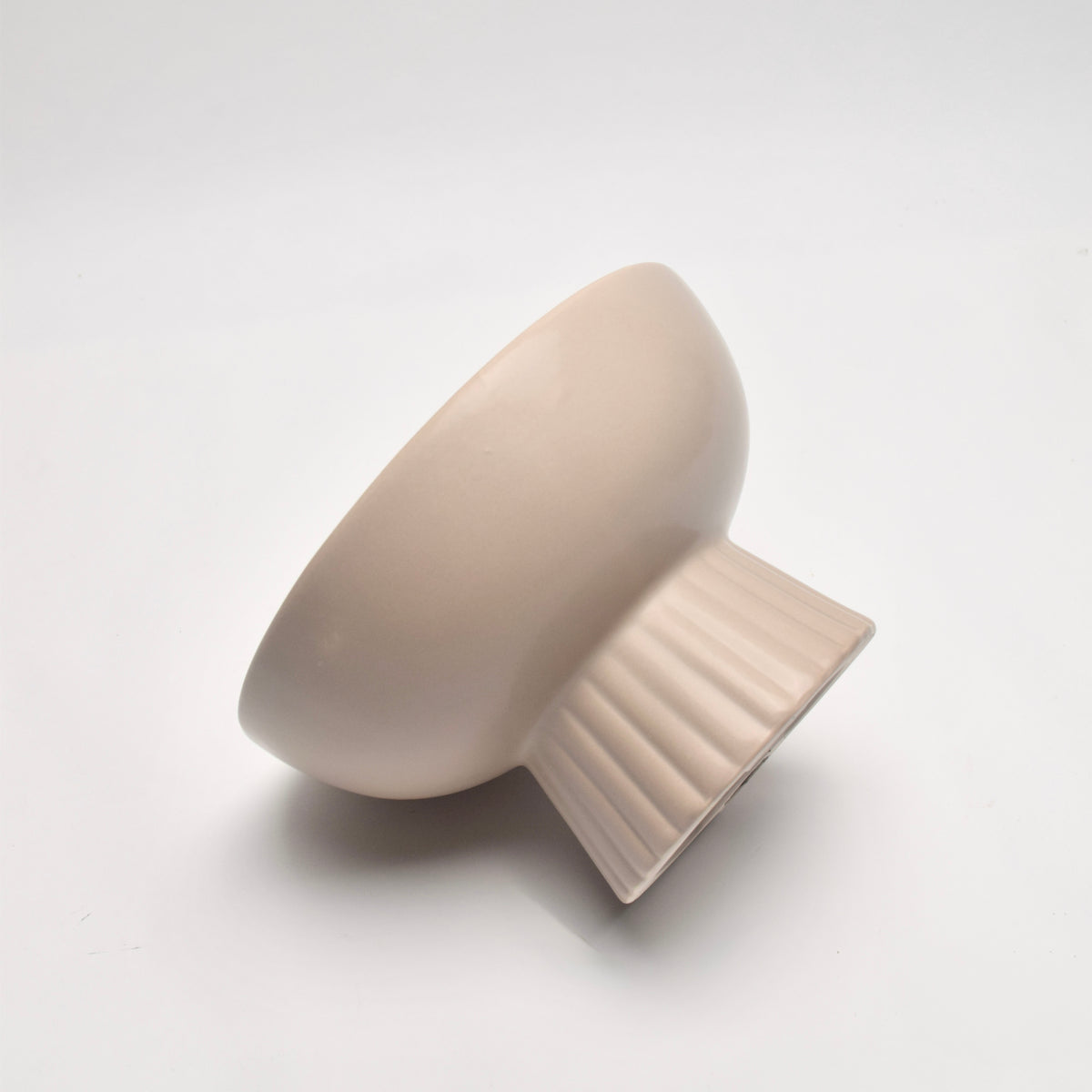 A minimalist ceramic bowl with a fluted pedestal base, finished in a matte warm off-white, photographed on studio background.