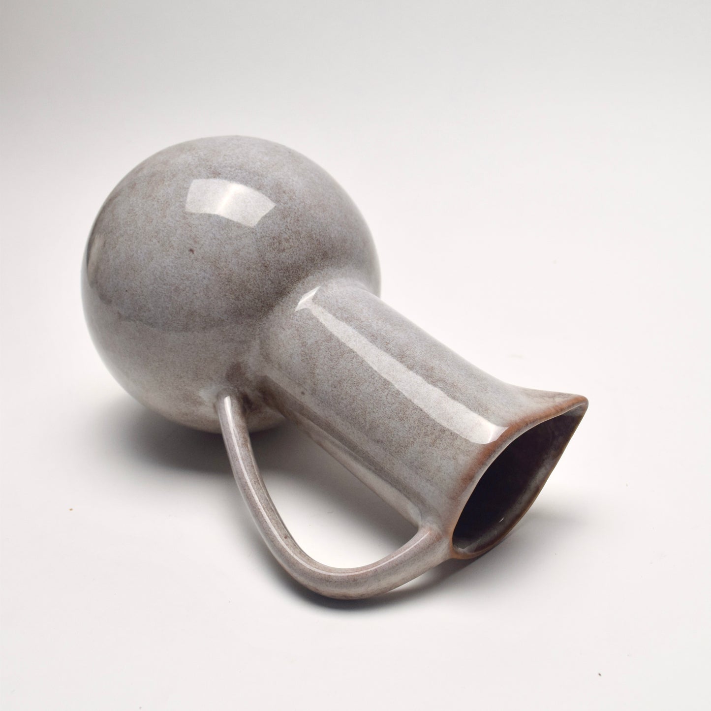 Grey ceramic glazed jug with speckled brown details, on its side