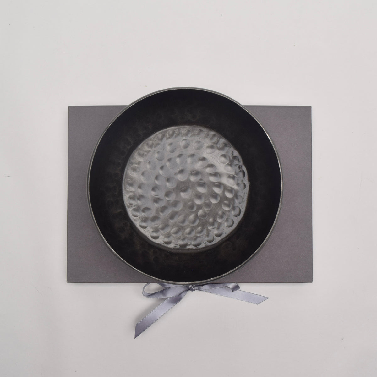 A hammered dark grey metal bowl  from above on top of grey book-style box