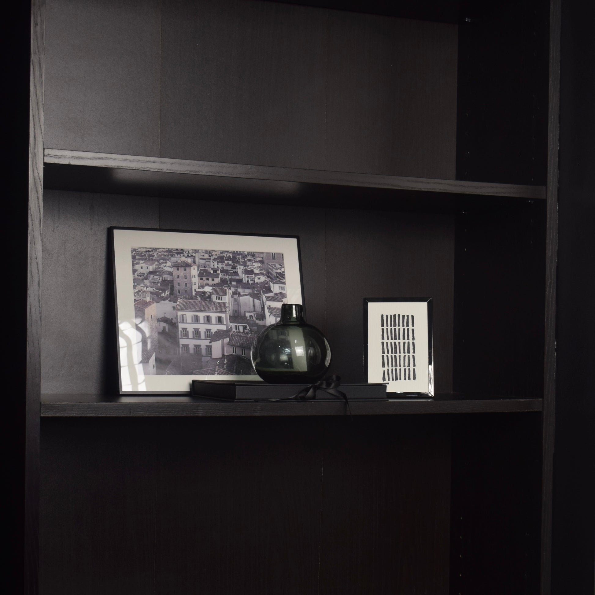 Framed artwork and decorative items on a black bookcase for shelf styling
