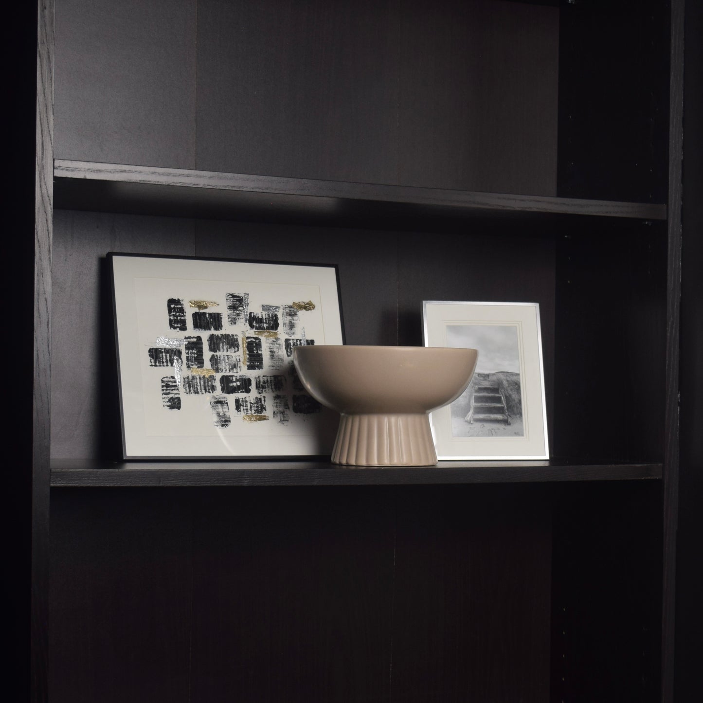 Decorative bowl and framed artwork on a black bookcase for shelf styling