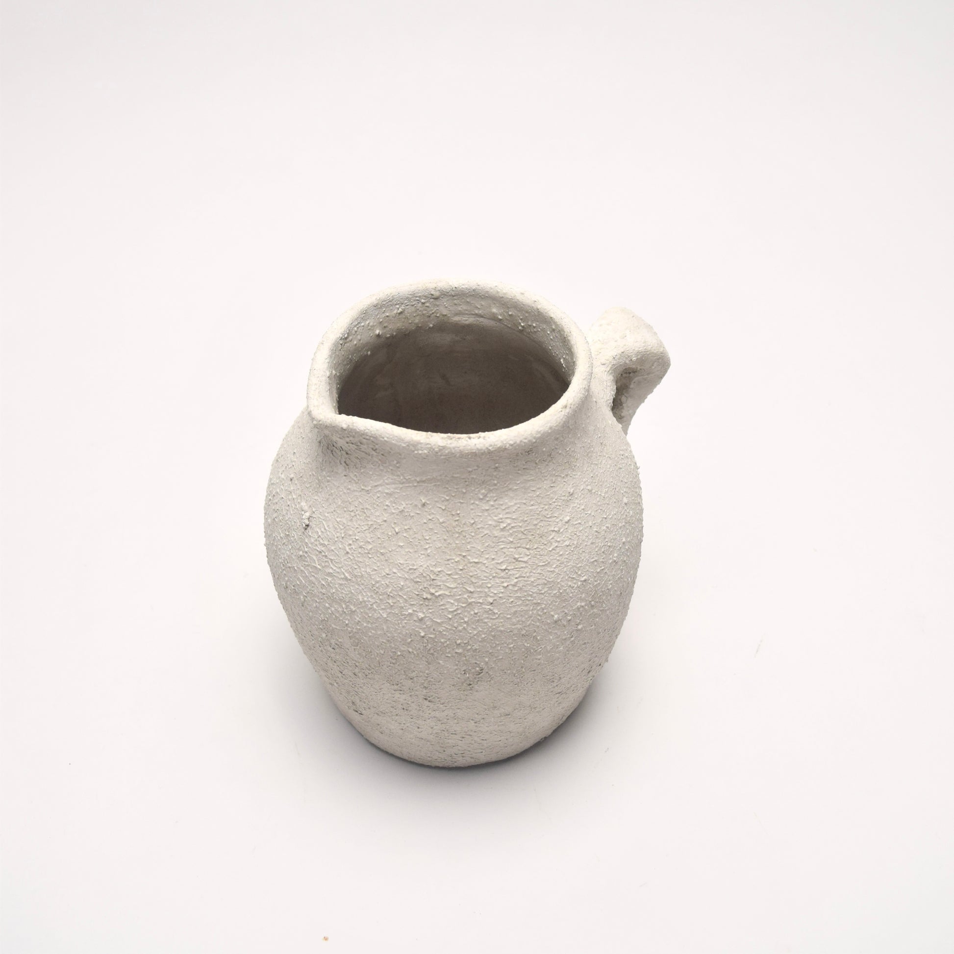 Small ceramic off-white vase with decorative handle and a textured surface 