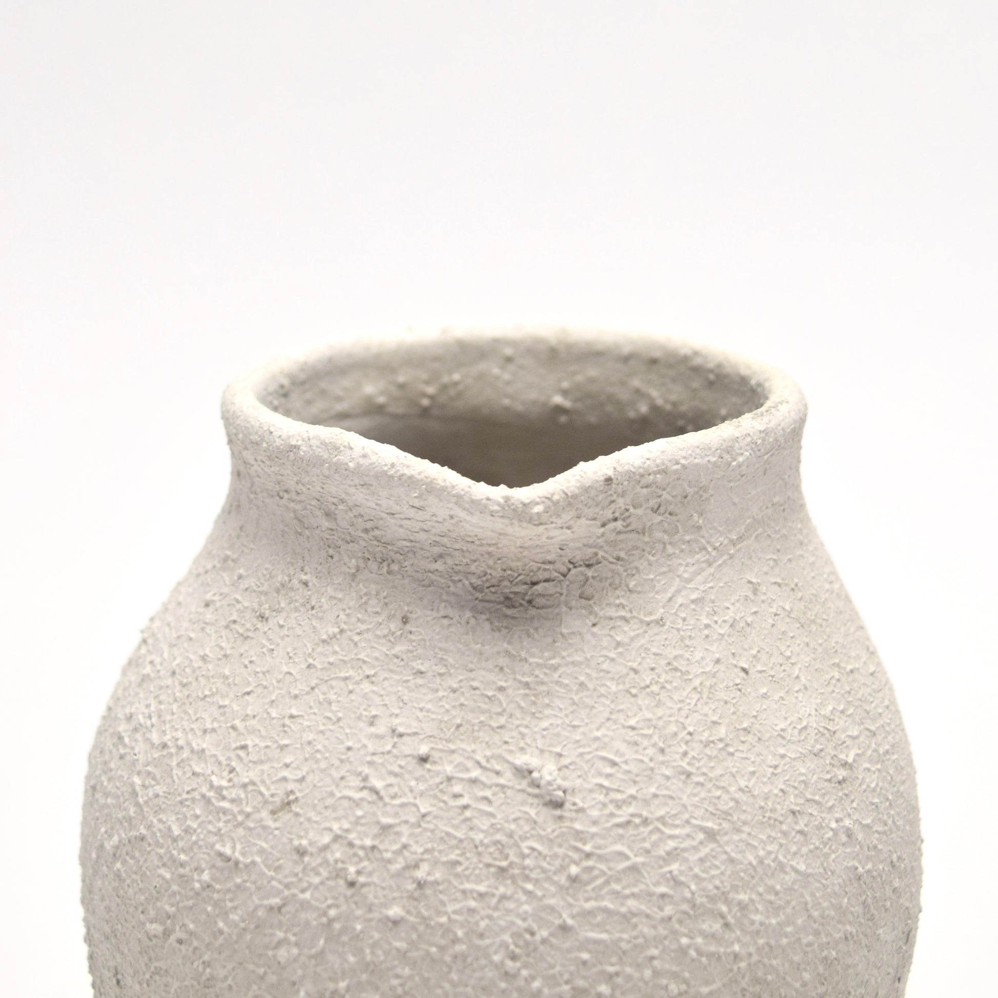 Close-up of the top of small ceramic off-white vase with a textured surface 