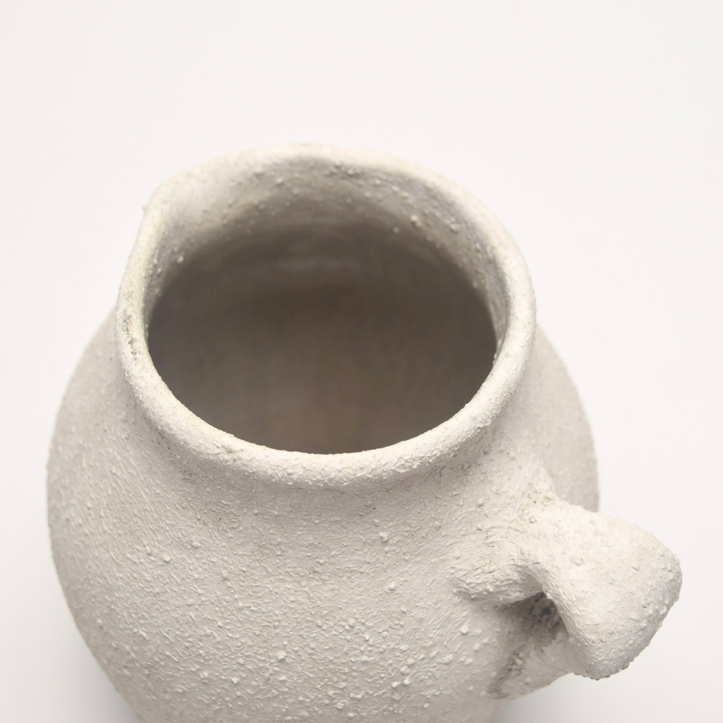 Textured ceramic pot with small handle at the back on a white background