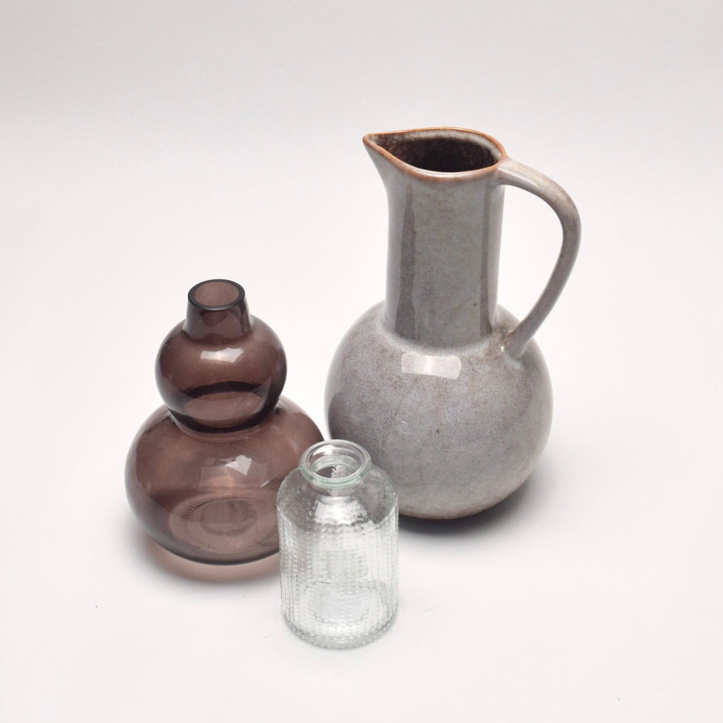 Set of 3 decorative vases for a gift, one ceramic glazed jug, one curved brown glass vase, and one dotted bud vase, perfect for shelf styling. 