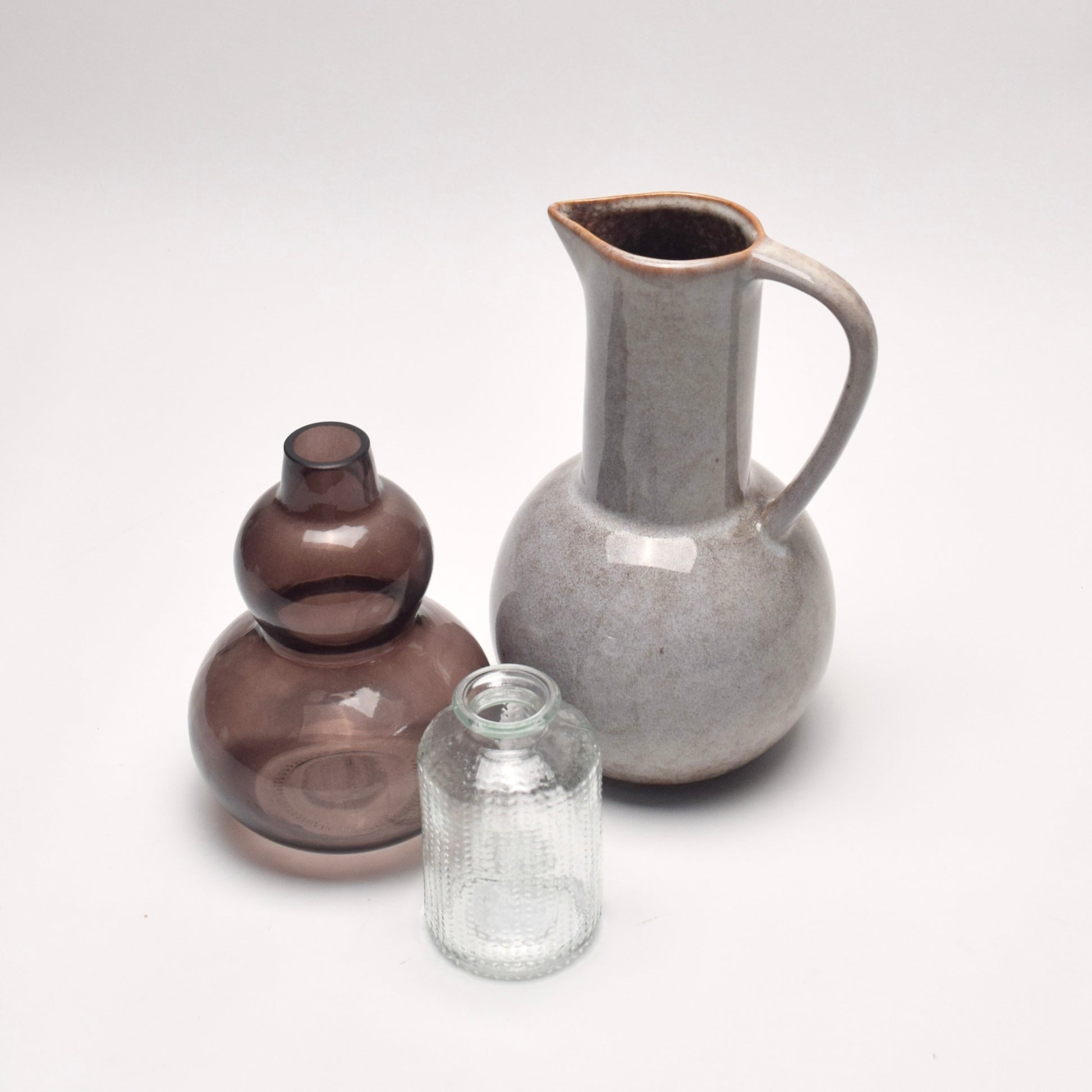 Set of 3 decorative vases for a gift, one ceramic glazed jug, one curved brown glass vase, and one dotted bud vase, perfect for shelf styling. 